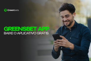 Greenbets APP - Conheça e Baixe o Aplicativo Grátis! Imagem com um homem de pele branca, usando fone de ouvidos, camisa social azul escura, sorrindo com o celular na mão em uma praça.